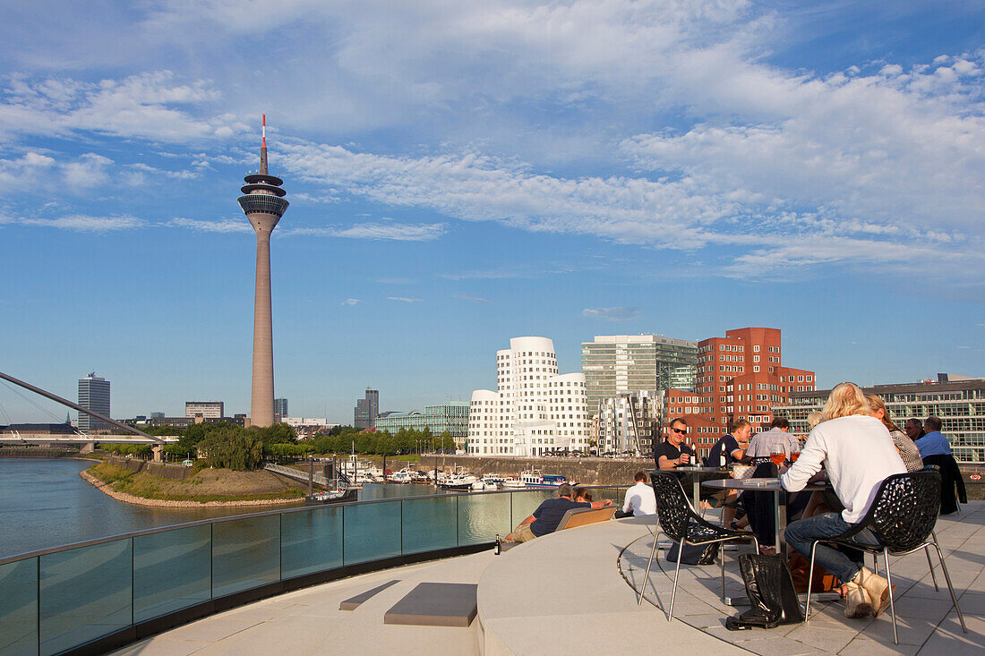 People at the terrace of a restaurant at media harbour, view to Rhine tower and Neuer Zollhof, Duesseldorf, North Rhine-Westphalia, Germany, Europe