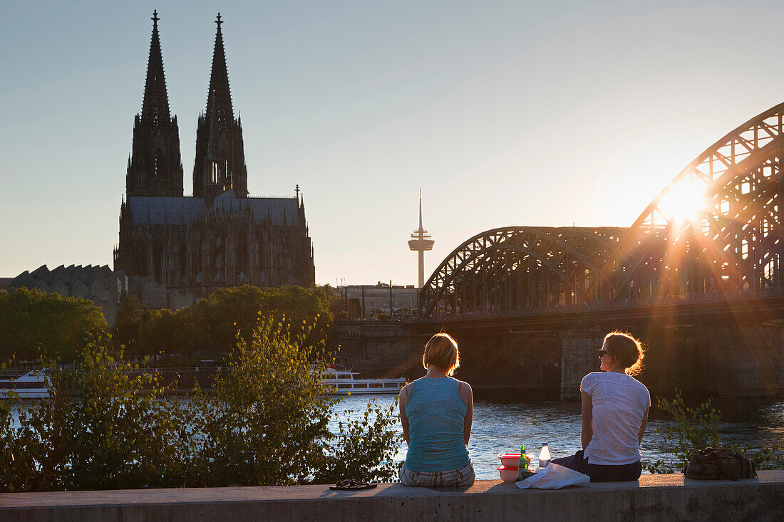 Young women sitting on the Rhine river banks opposite to the cathedral, Cologne, North Rhine-Westphalia, Germany, Europe