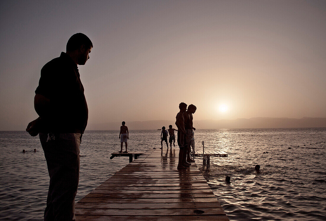 Vater beobachtet Kinder beim Schwimmen, Sonnenuntergang am Golf von Akaba, Rotes Meer, Jordanien, Naher Osten, Asien
