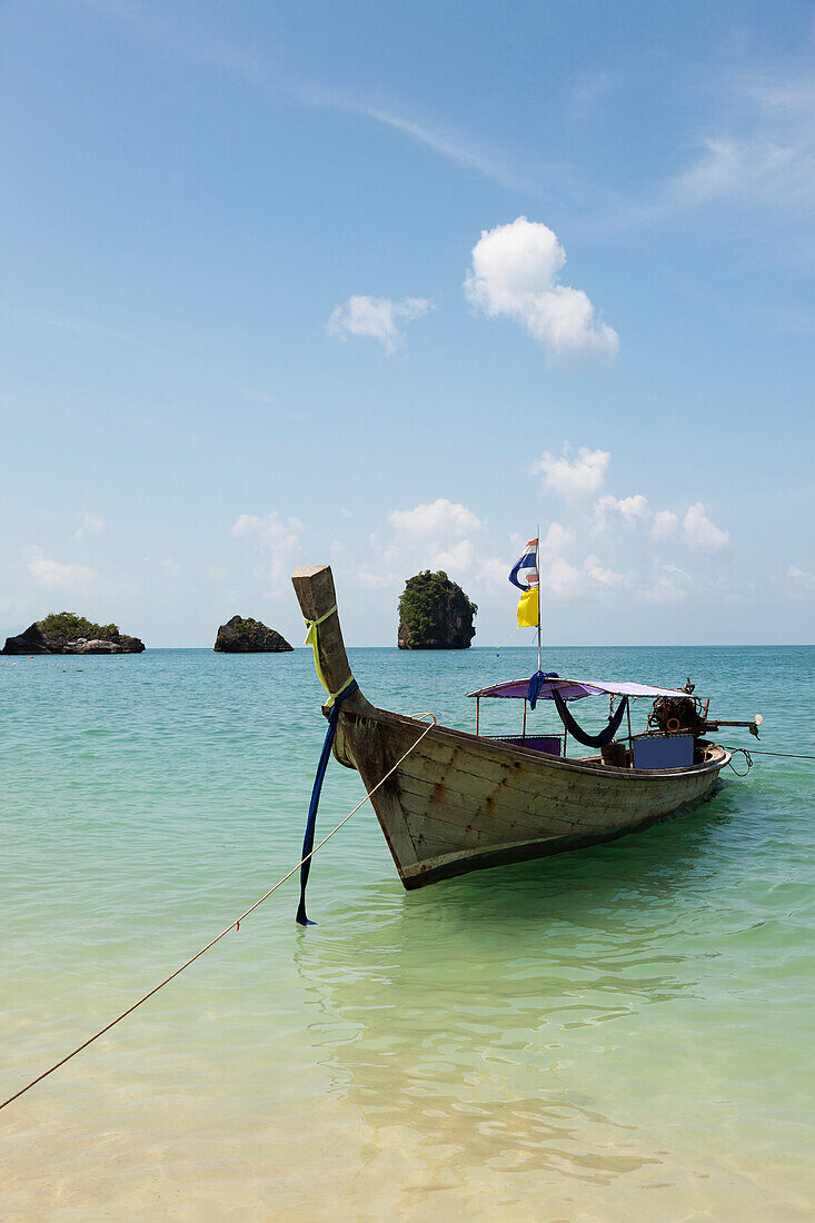 A traditional long tail boat moored in shallow water on Tham Phra Nang beach. Landscape sea pillars and limestone karsts rising up from the sea water., Rai Leh, Krabi Province Thailand.