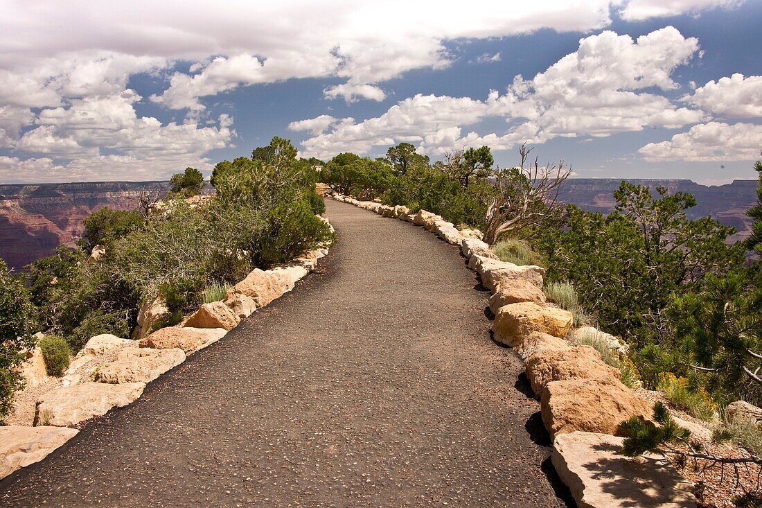 A paved walkway leads to the precipice overlooking the Grand Canyon