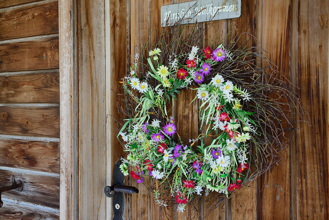Wreath of flowers hanging on a wooden door at an old farmhouse, Strassberg, Walserweg, Arosa, Grisons, Switzerland