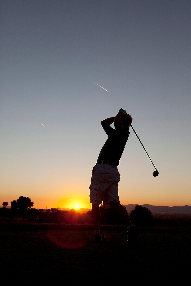 Golfer schlägt den Ball bei Sonnenuntergang ab