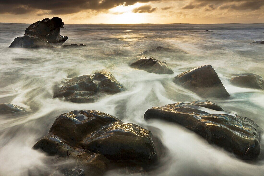 Sun sets beneath heavy cloud layer, seascape on rocks off Gillespie´s Beach, Westland National Park, West Coast