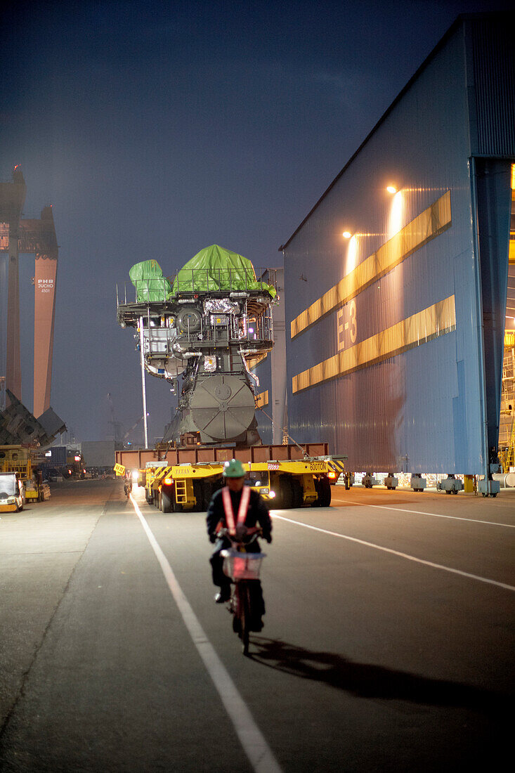Moped driver leading a giant flatbed truck that is transporting MAN two-stroke engine from the test bed to the dry-dock, modular production at the laargest shipyard in the world, Hyundai Heavy Industries, HHI, in Ulsan, South Korea, Asia