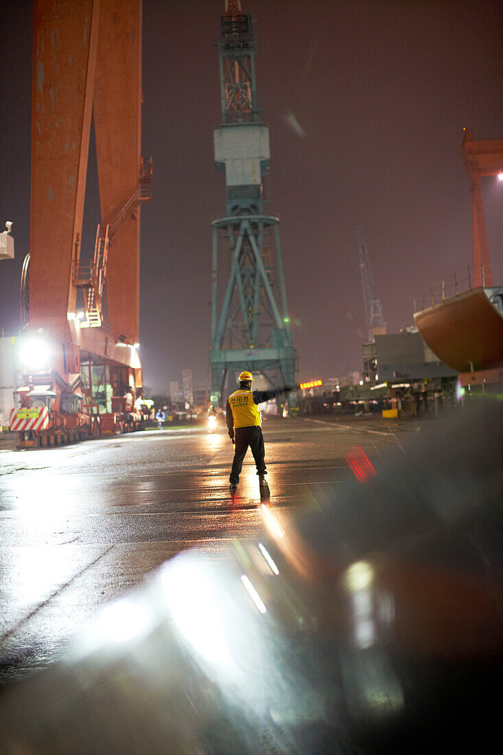 Sicherheitsmann regelt den Verkehr abends auf weltgrößter Schiffswerft, Hyundai Heavy Industries (HHI) Werft, Ulsan, Südkorea