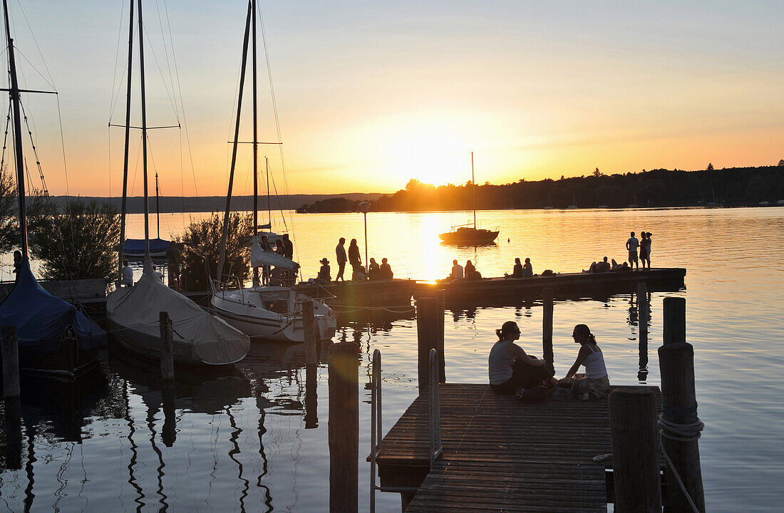 Menschen auf einem Steg am Ammersee bei Sonnenuntergang, Herrsching, Oberbayern, Bayern, Deutschland, Europa