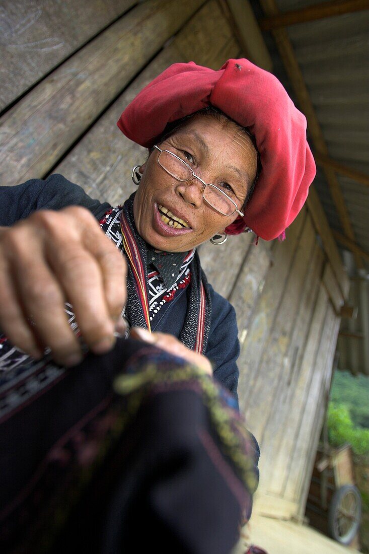 Red Zao hilltribe woman with spectacles sewing Ta Phin village near Sapa town north Vietnam