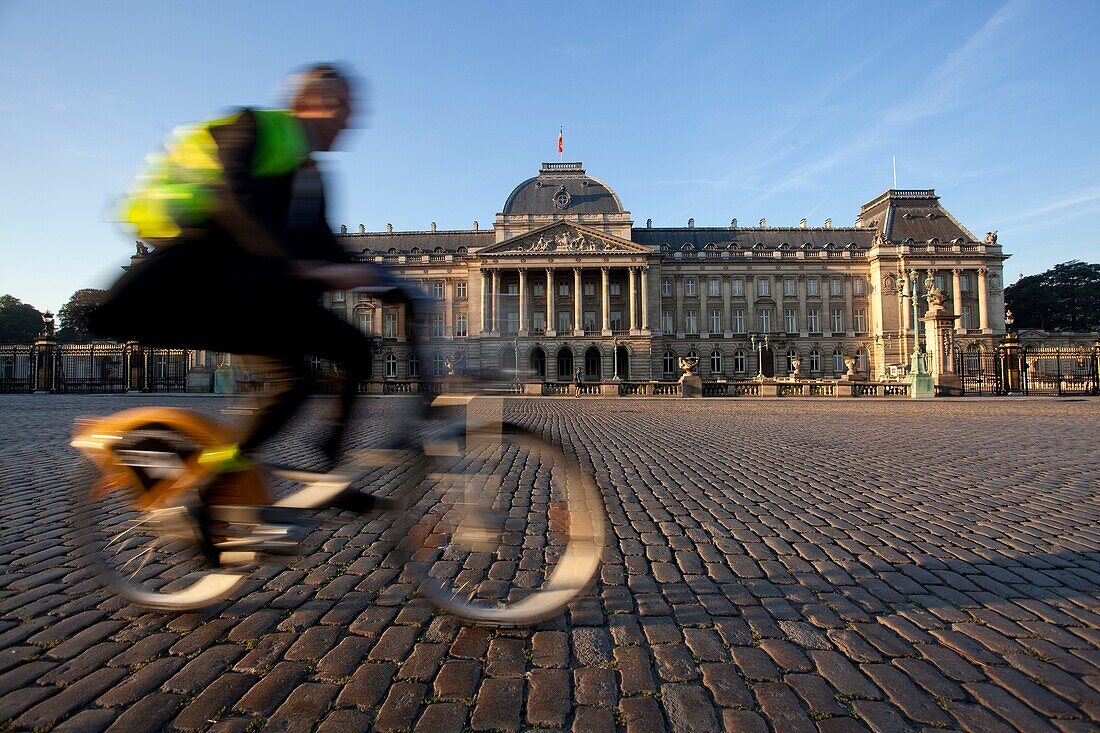 A man rides a bike next to the Royal Palace in Brussels, Belgium