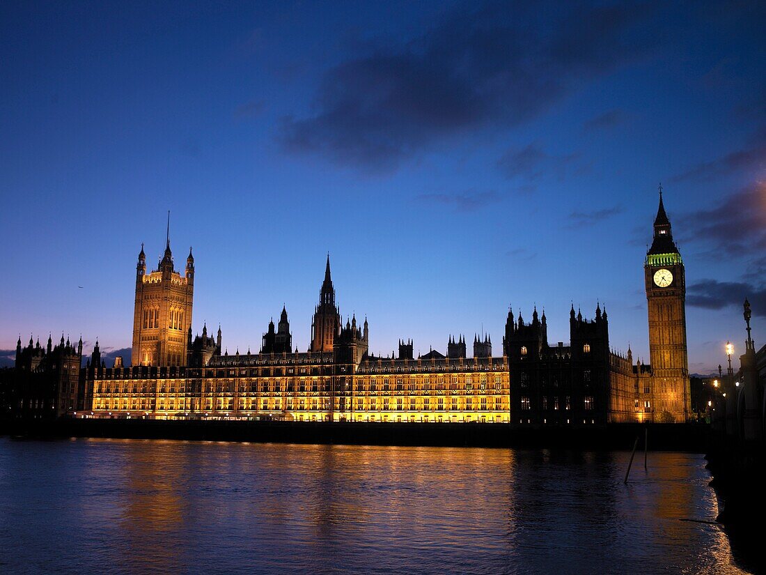 An illuminated Big Ben, Victoria Tower and the Houses of Parliament seen from across the River Thames