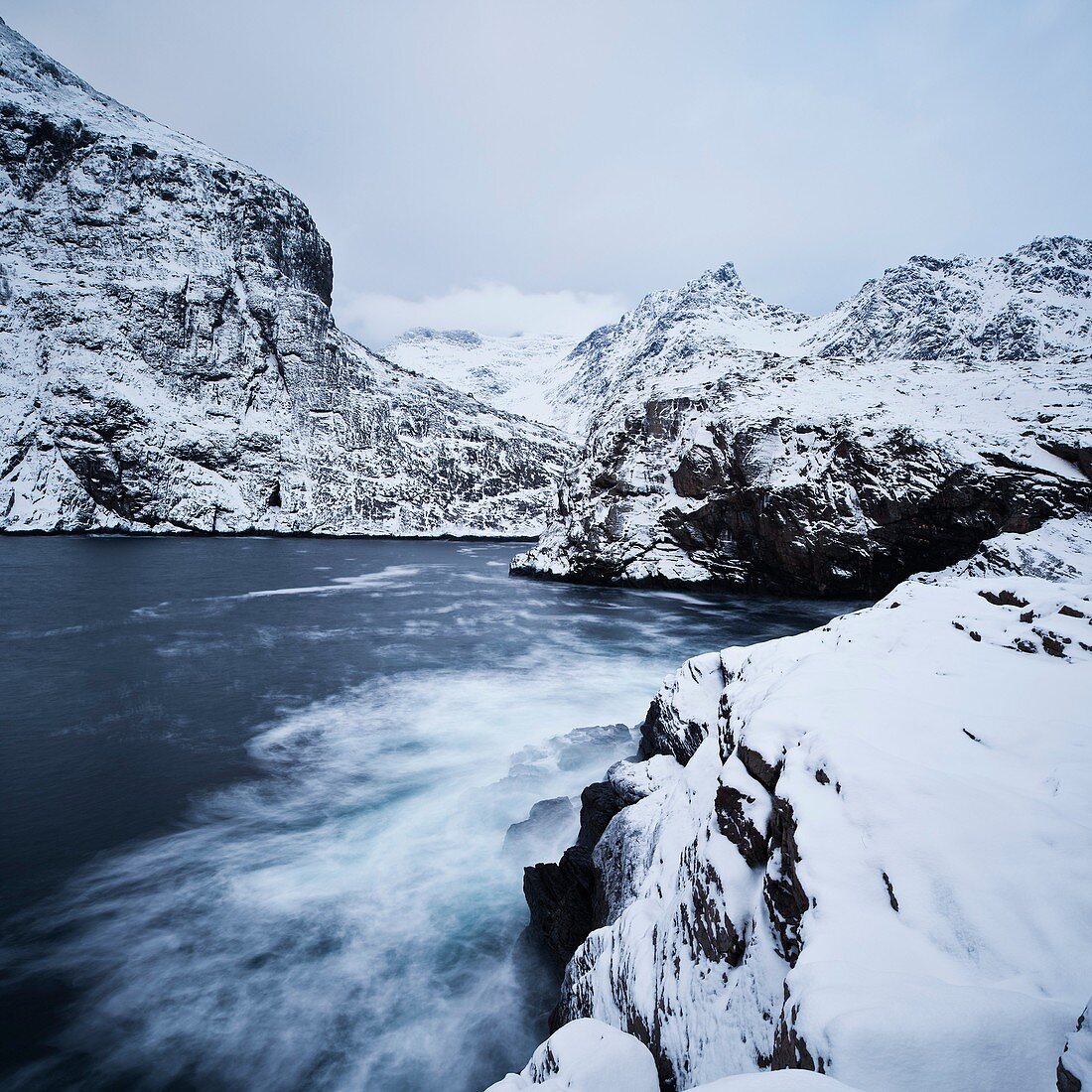 Snow covered cliffs and mountains rise from sea, Å I Lofoten, Lofoten Islands, Norway
