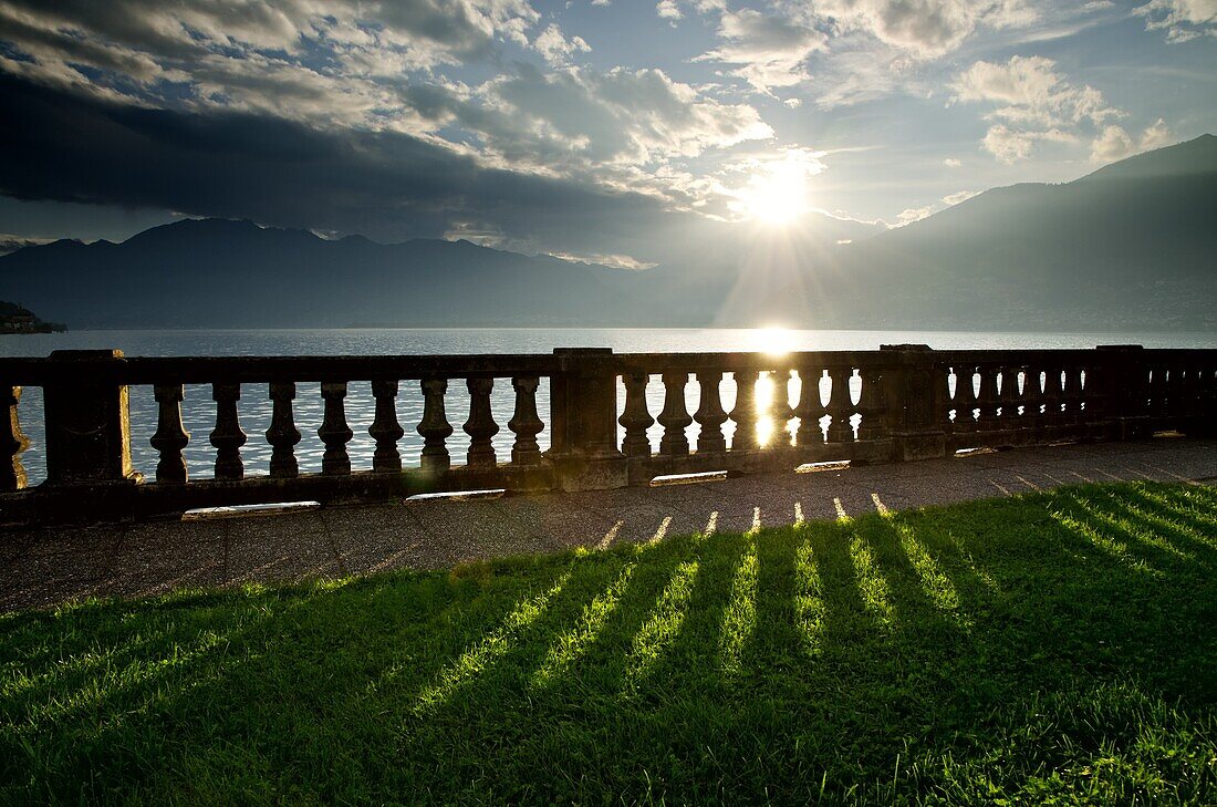 Sunlight on the lake front with fence and shadow and mountains with clouds