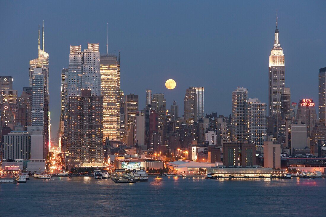 The full moon rises over the Manhattan skyline at twilight as viewed over the Hudson River from New Jersey