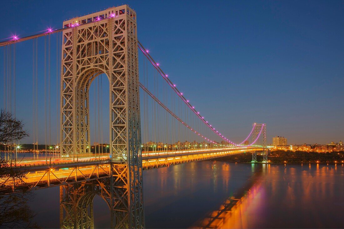 The George Washington Bridge, with pink lights in support of National Breast Cancer Awareness Month, spanning the Hudson River shortly after sunset in New York City, New York, USA.