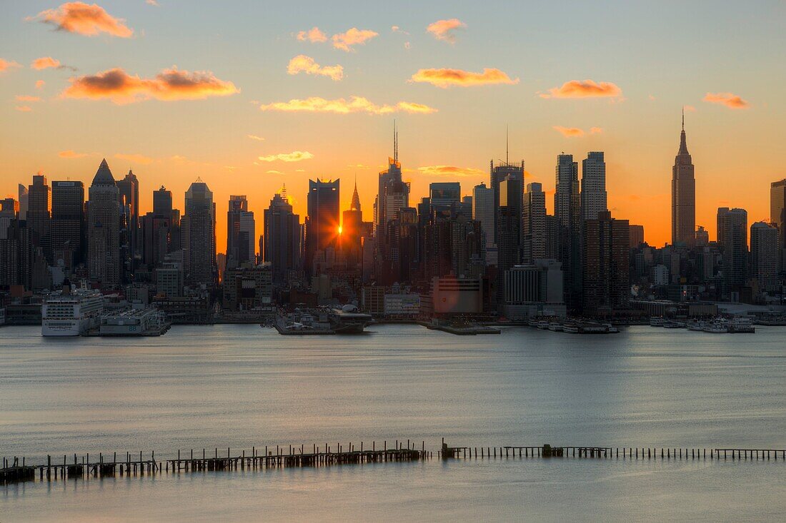 The rising sun shines through the buildings of the Manhattan skyline in New York City a few minutes after sunrise as viewed over the Hudson River looking east from New Jersey.
