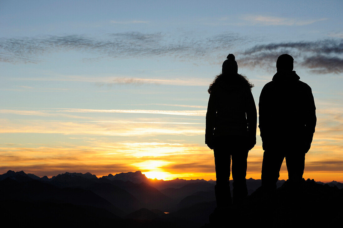 Junge Frau und junger Mann genießen Sonnenuntergang am Gipfel des Risserkogel, Bayerischen Voralpen, Mangfallgebirge, Bayern, Deutschland