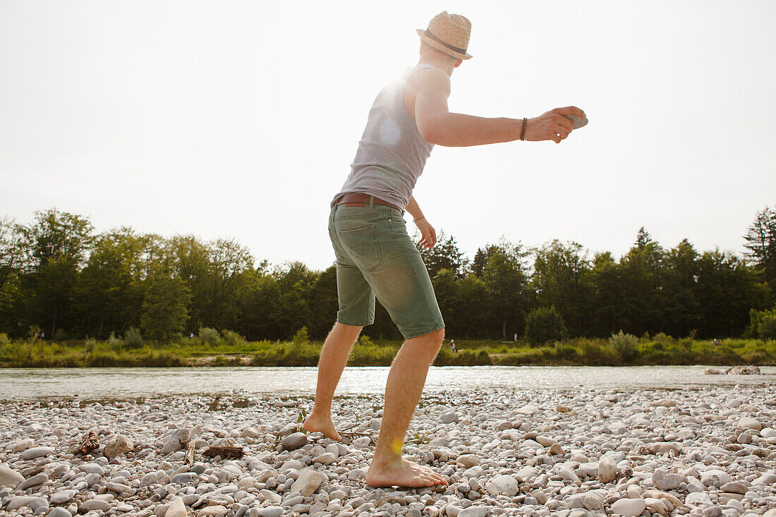 Junger Mann wirft Steine an der Isar, München, Bayern, Deutschland