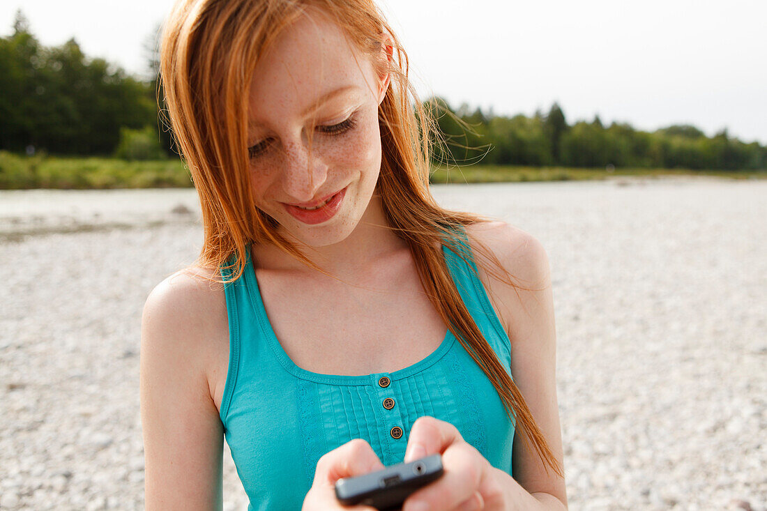 Junge Frau mit einem Handy an der Isar, München, Bayern, Deutschland
