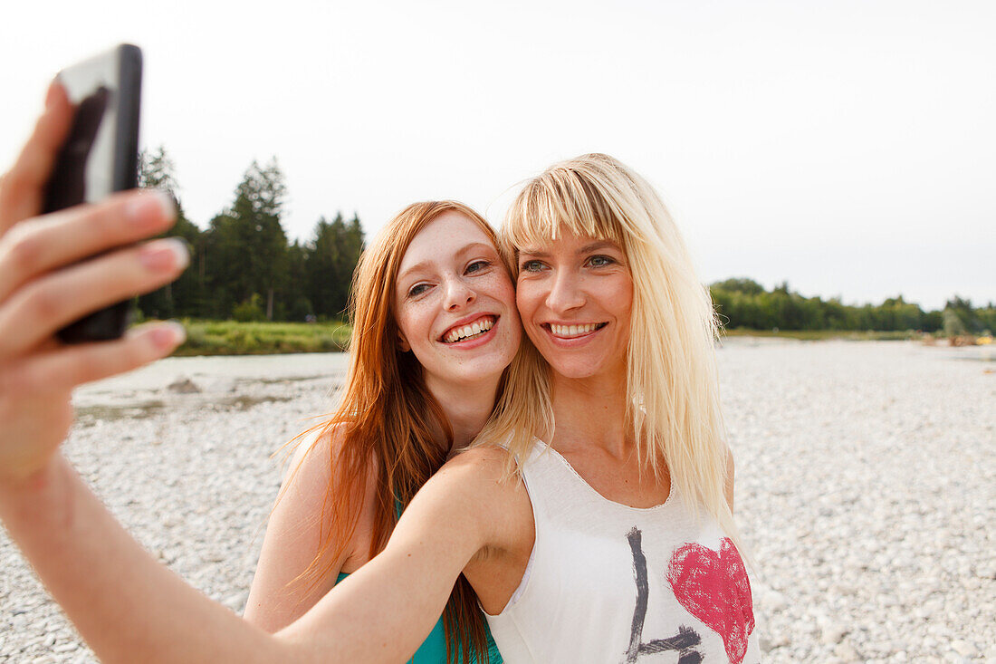 Two young women taking pictures of themselves by a mobile phone, Munich, Bavaria, Germany