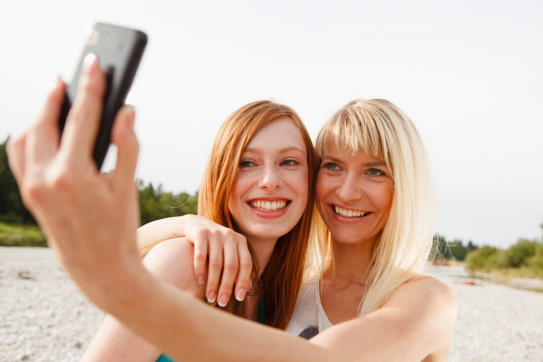 Two young women taking pictures of themselves by a mobile phone, Munich, Bavaria, Germany