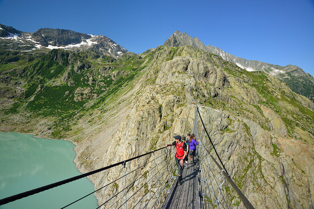 Hikers walking over a suspension bridge across a mountain lake, Trift glacier, Trift suspension bridge, Tieralplistock, Urner Alps, Bernese Oberland, Bern, Switzerland