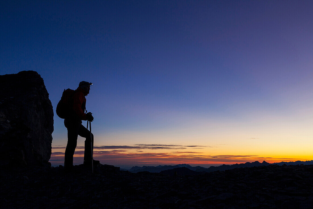 Ein Mann beim Wandern mit Stirnlampe in der Morgendämmerung auf dem Wandergipfel der Wilden Frau, Berner Oberland, Kanton Bern, Schweiz