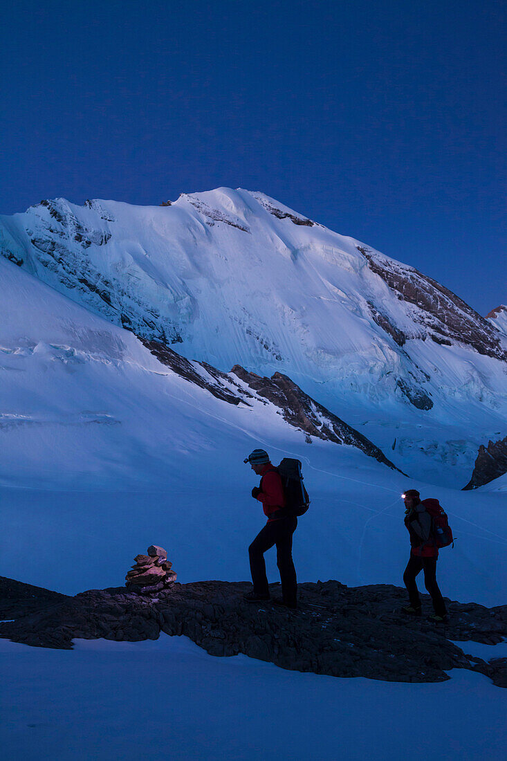 Ein Mann und eine Frau beim Wandern mit Stirnlampe im Aufstieg in der Morgendämmerung zum Wandergipfel der Wilden Frau, Blick zum Blüemlisalpmassif, Blüemlisalphorn, Berner Oberland, Kanton Bern, Schweiz