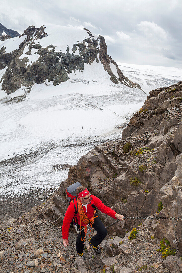 A male mountaineer, ascending along chains to the saddle of Gamchiluecke, view to Tschingelfirn glacier and Mount Mutthorn, Bernese Oberland, Canton of Bern, Switzerland