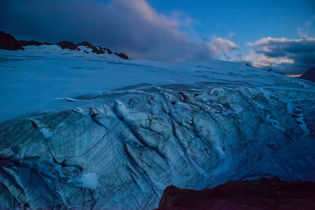 Two roped parties of mountaineers on Kanderfirn glacier in the moonlight in the distance, walking from Mutthorn hut to Petersgrat, Bernese Oberland, Canton of Bern, Switzerland