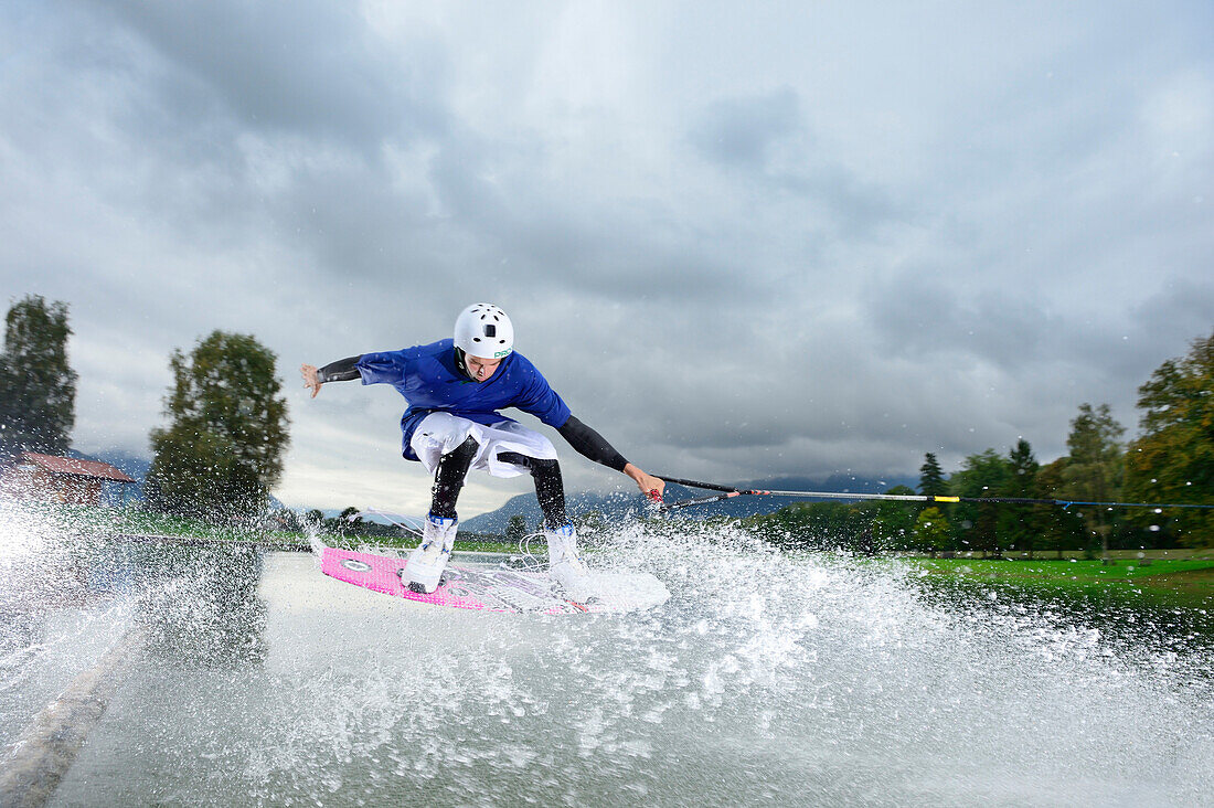 Young man surfing on wakeboard, wakeboarding at lake Neubeurer See, Neubeuern, Rosenheim, Upper Bavaria, Bavaria, Germany