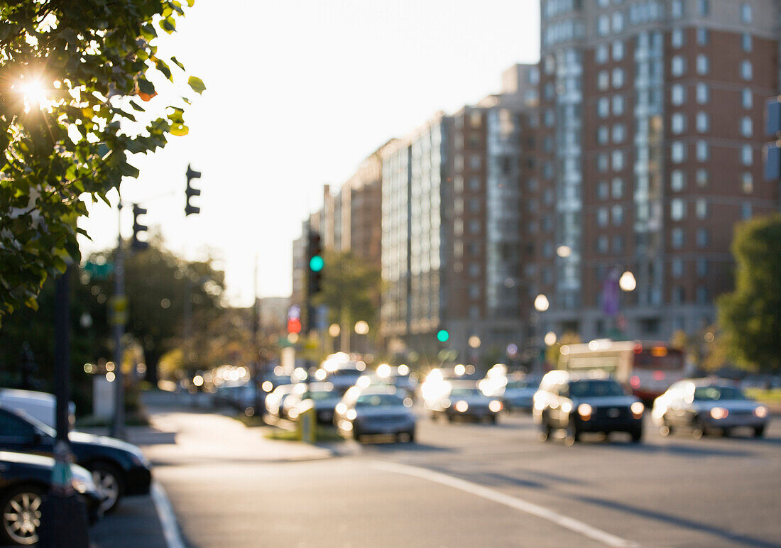 Out of focus street scene in Washington DC at sunrise. Green traffic lights and traffic moving along the road. Buildings.
