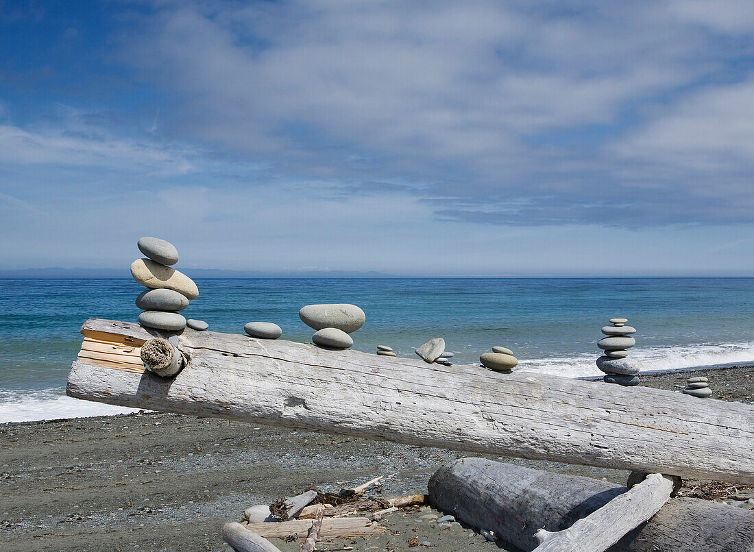 Dungeness Spit near Sequim, a view over the sea, from the beach. A pile of wood, with small stacks of rocks balanced on a wooden log.