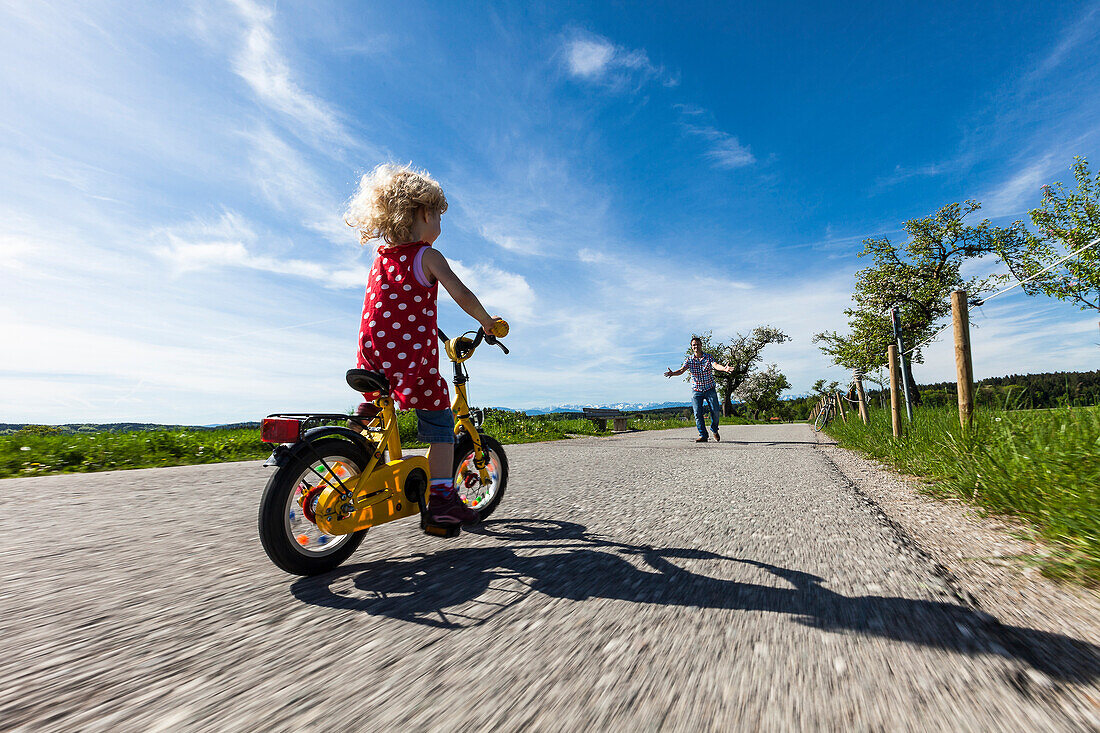 Mädchen fährt Fahrrad, Vater im Hintergrund, Oberbayern, Bayern, Deutschland