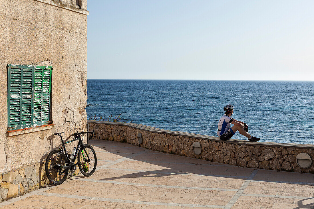 Bicycle rider resting on a mall at Mediterranean coast, Sant Elm, Majorca, Balearic Islands, Spain