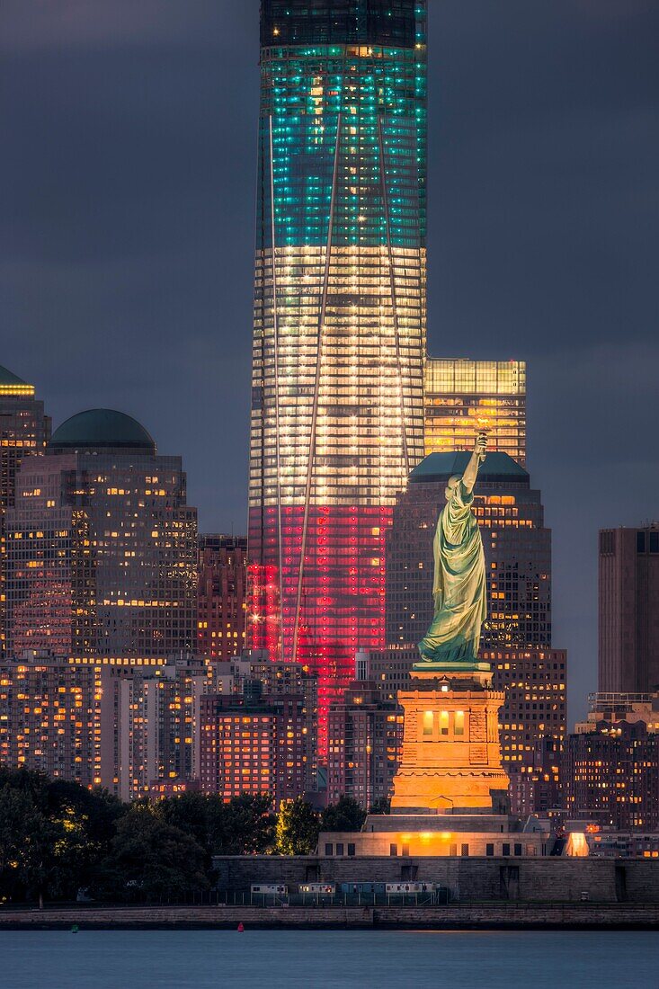 Two symbols of freedom, the Statue of Liberty and the Freedom Tower One World Trade Center, are illuminated at twilight in New York City. The Freedom Tower, lighted in the red, white, and blue colors of the American flag, is scheduled for completion in 20