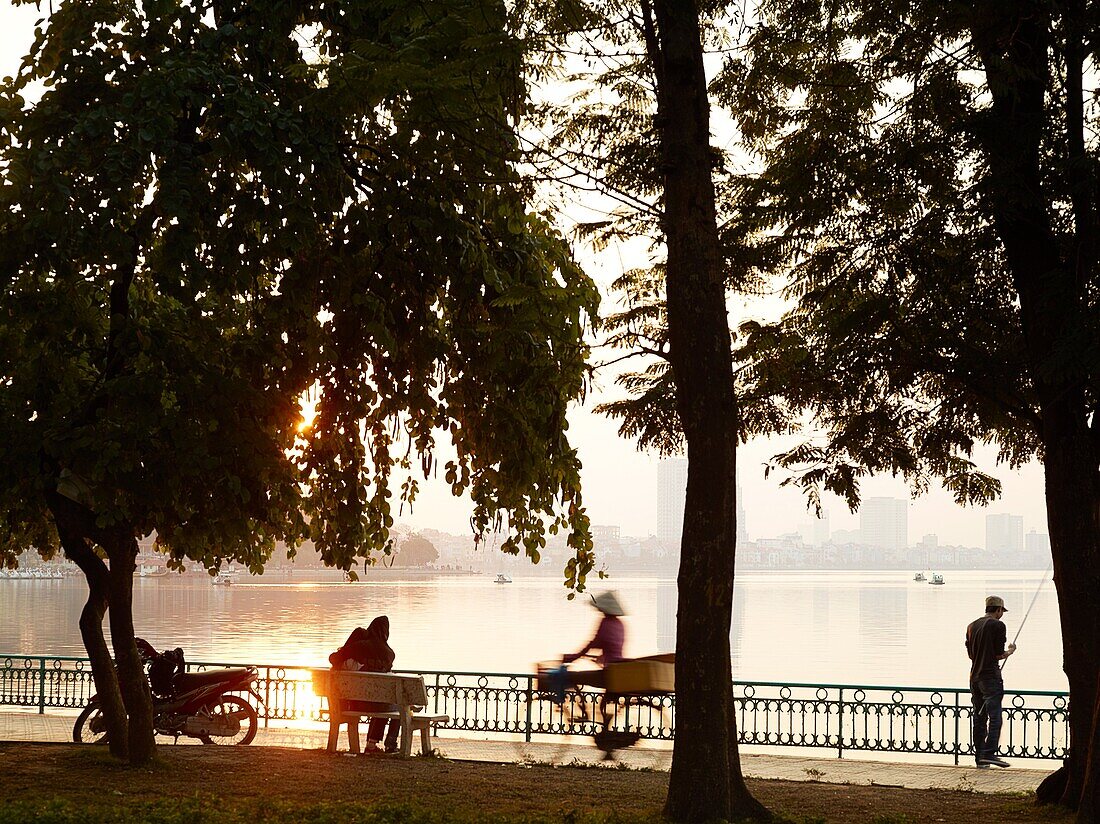 A young couple embraces on a park bench overlooking Hanoi´s West Lake, one of the few natural escapes within the bustling city  Their parked motorbike and a fisherman are nearby   Vietnam is underging a major economic transformation, throwing the youth of