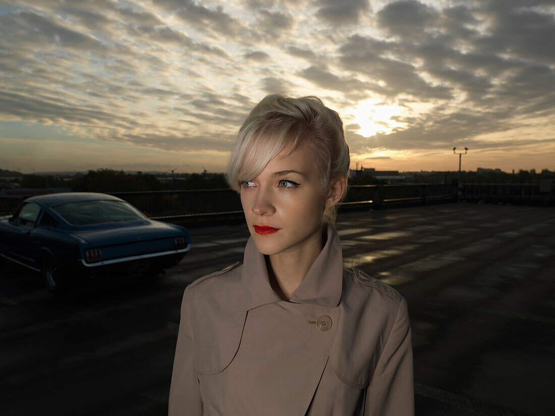 Businesswoman walking in parking lot. Sunrise in car park with car in back ground and girl in coat in foreground