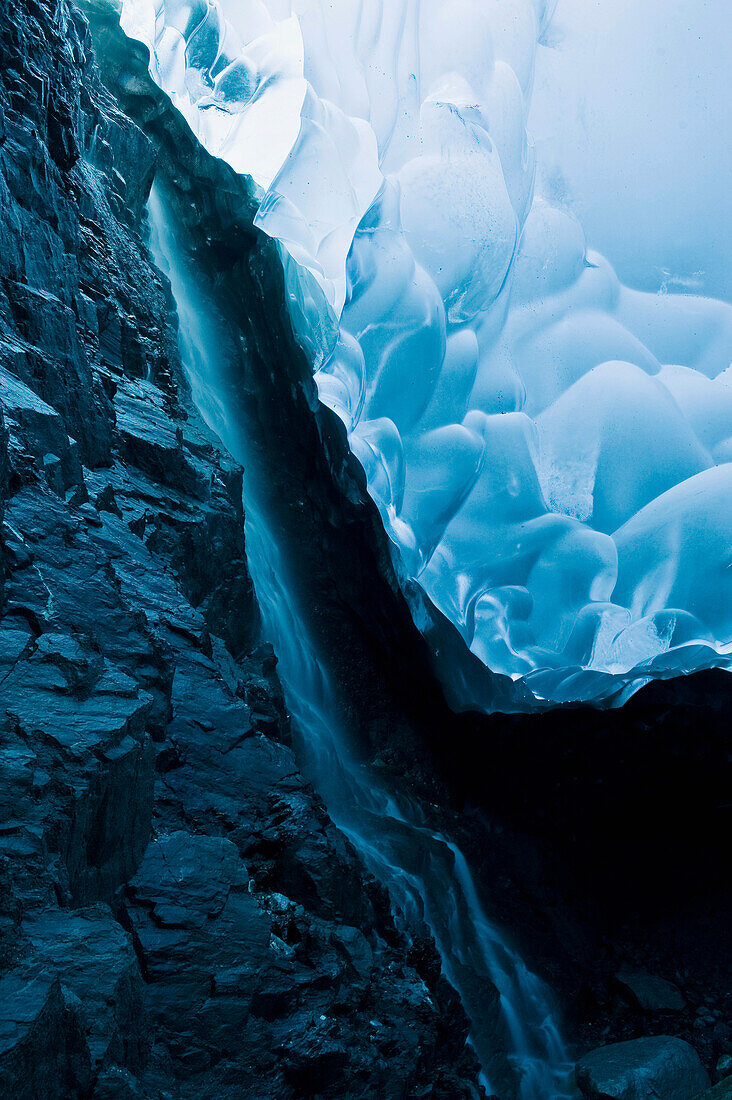 A waterfall trickles its way down the rock face of an ice cave inside the Mendenhall Glacier, Juneau, Southeast Alaska, Summer