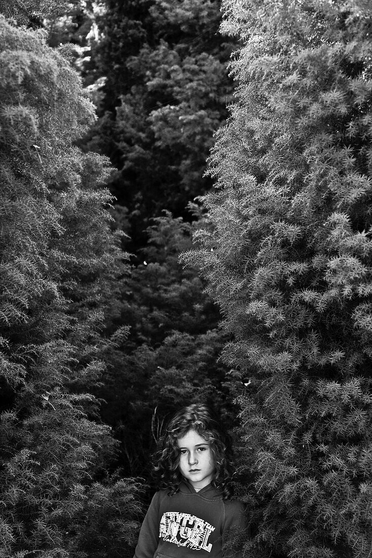 Young Girl With Curly Hair Standing Amongst Tall Trees, Portrait