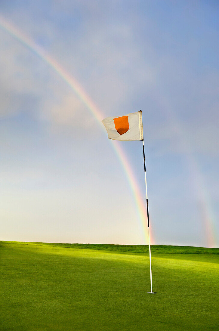 Rainbow falling onto putting green and golf pin, summer, daytime