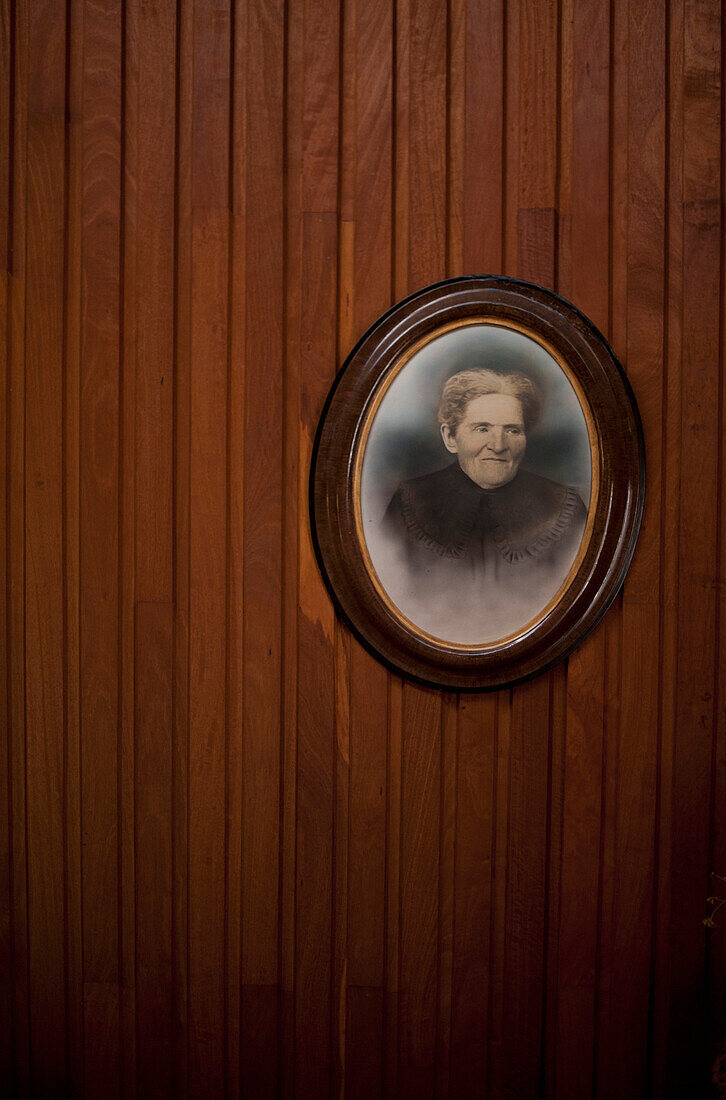 A historic hand tinted photograph, a portrait of a woman. Ancestor. Family history. Wooden wall.