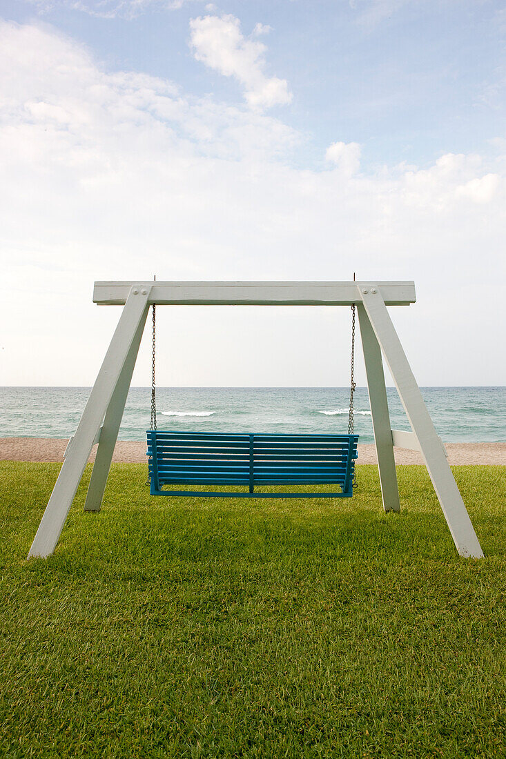 A wooden beach swing with a green painted seat. A good view of the sea.