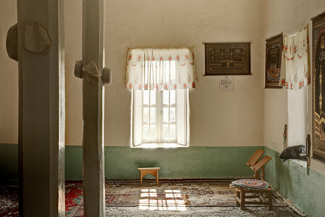 The interior of a village mosque, with carpets laid on the floor and pillars and signs and pictures on the wall. Caucusus mountains.