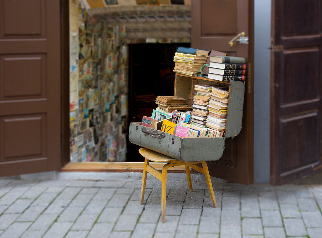 An antique shop on a street in a town in Estonia. A suitcase of second hand books in a suitcase on a chair.