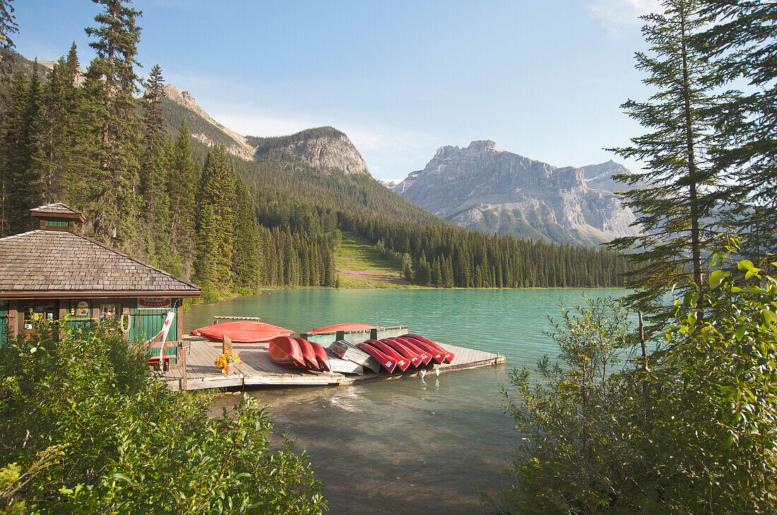 A view from a waterfront pier over the landscape of the Rocky Mountains surrounding the Emerald Lake and the brightly coloured waters of the lake, Canoes and kayaks for hire