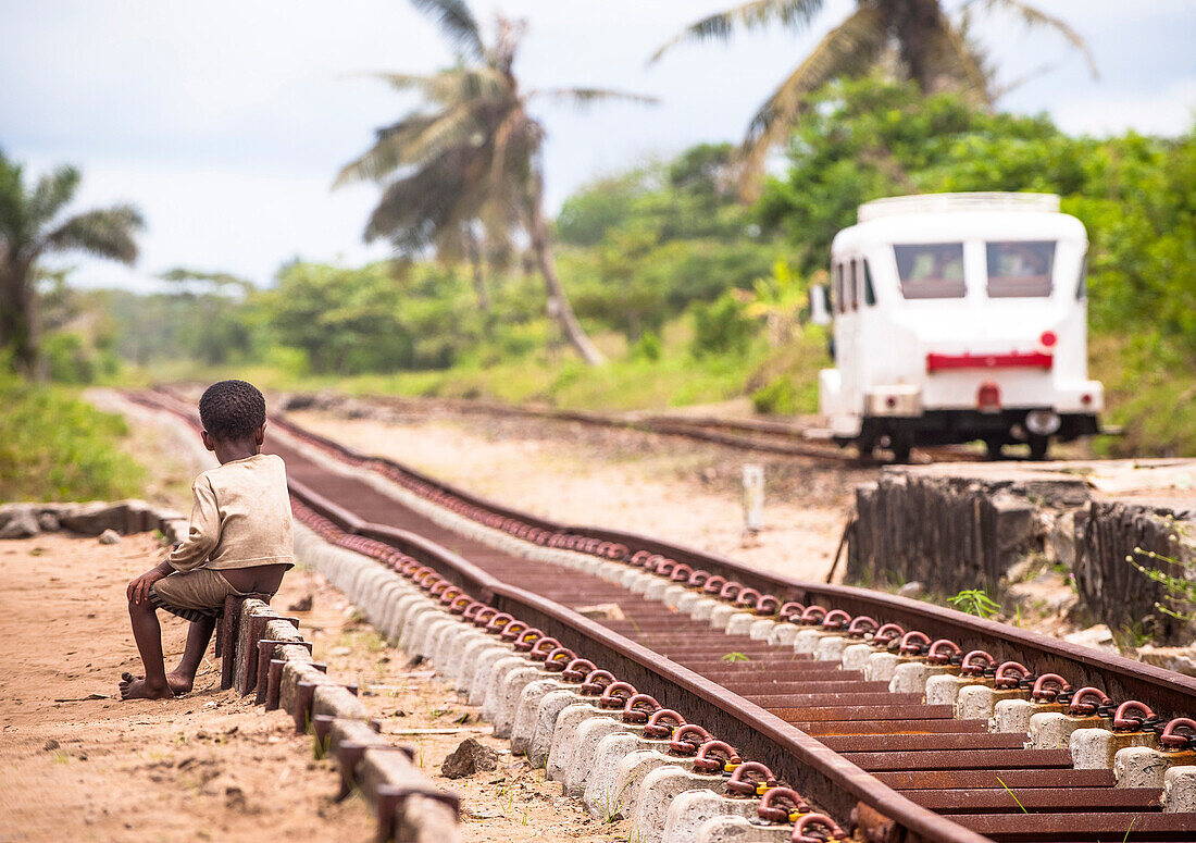 Kind sitzt am Schienenrand und beobachtet Züge, Madagaskar, Afrika