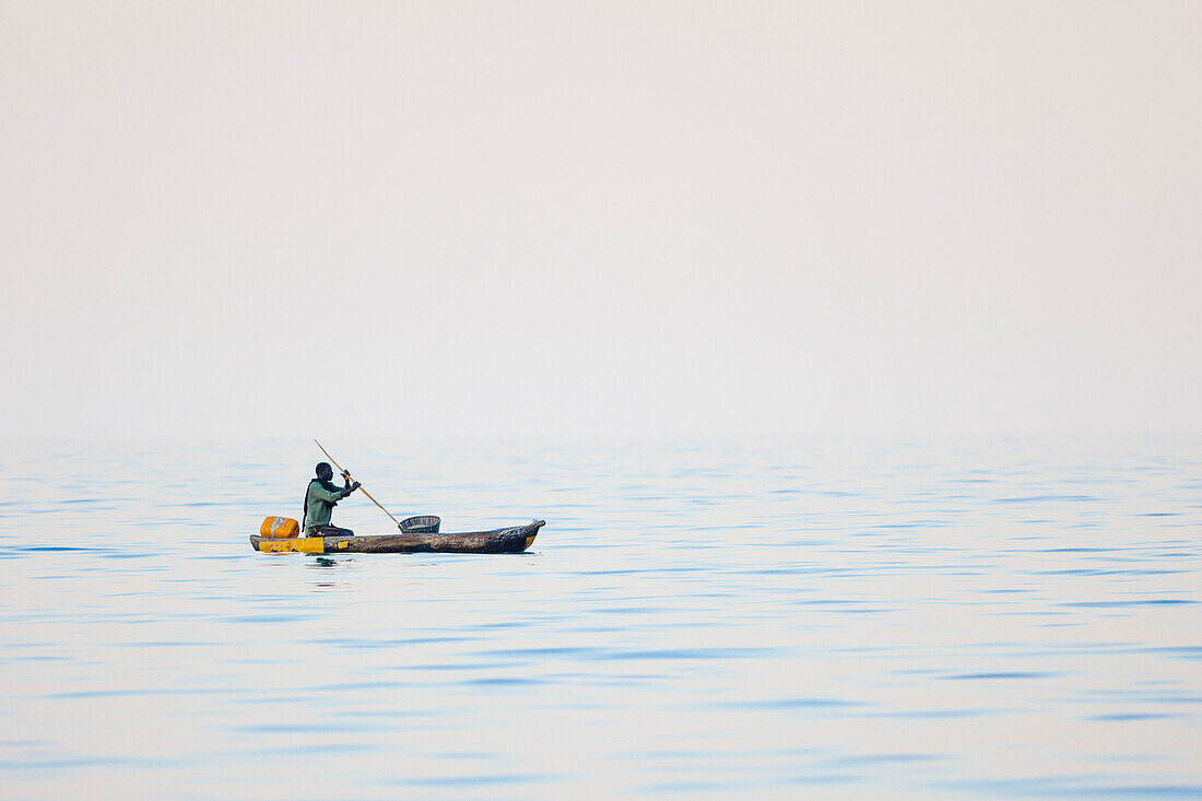 Ein Mann paddelt mit einem Einbaum, Holzkanu, auf dem Malawi See, Malawi, Afrika
