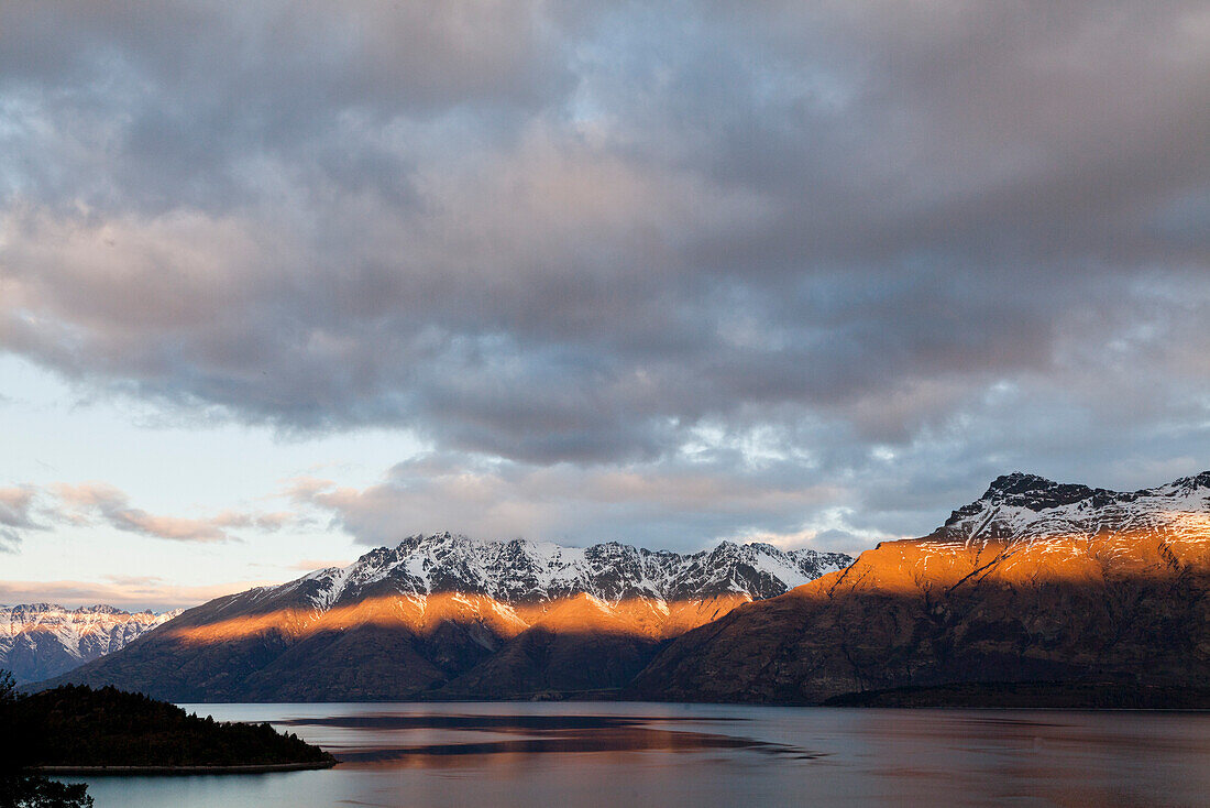 letzte Lichtstrahlen der untergehenden Sonne auf einem Gebirgszug am Lake Wakatipu,Bergkulisse bei Queenstown,Streiflicht,Wolkenspalte,Queenstown,Südinsel,Neuseeland