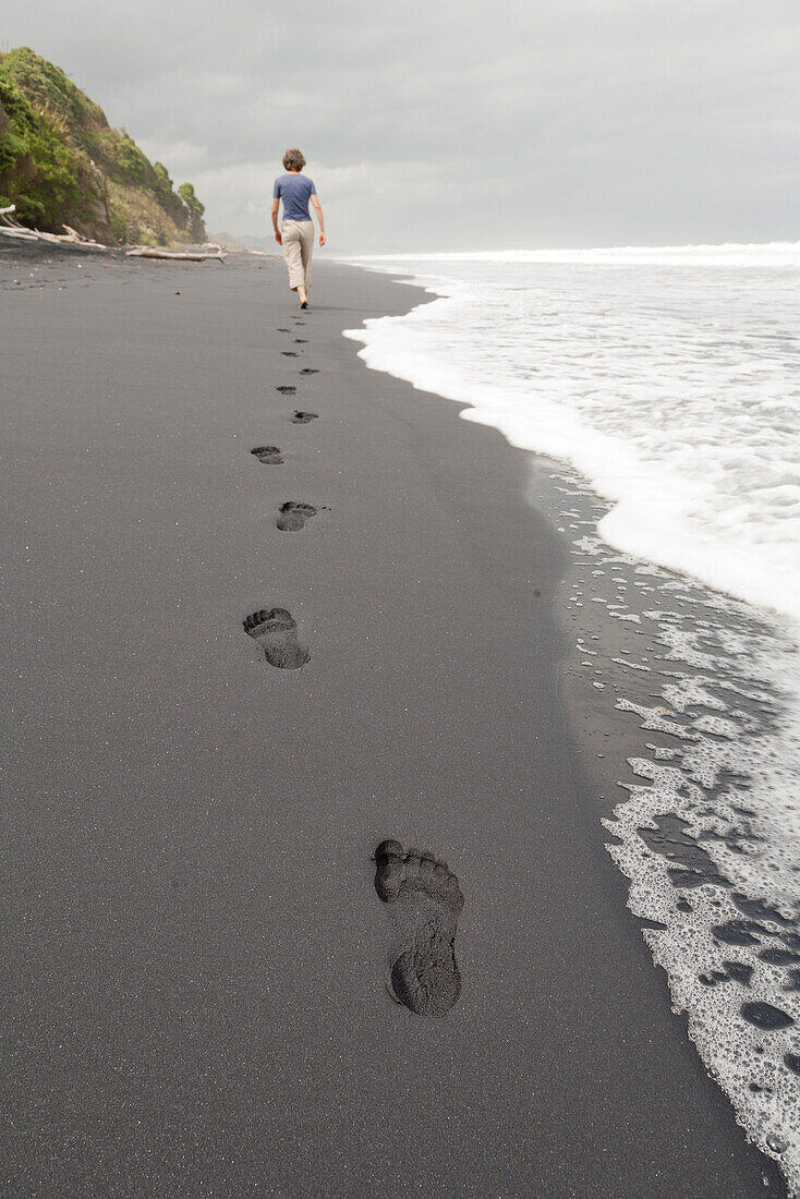 Footprints in black sand, woman walking along the beach, South Island, New Zealand