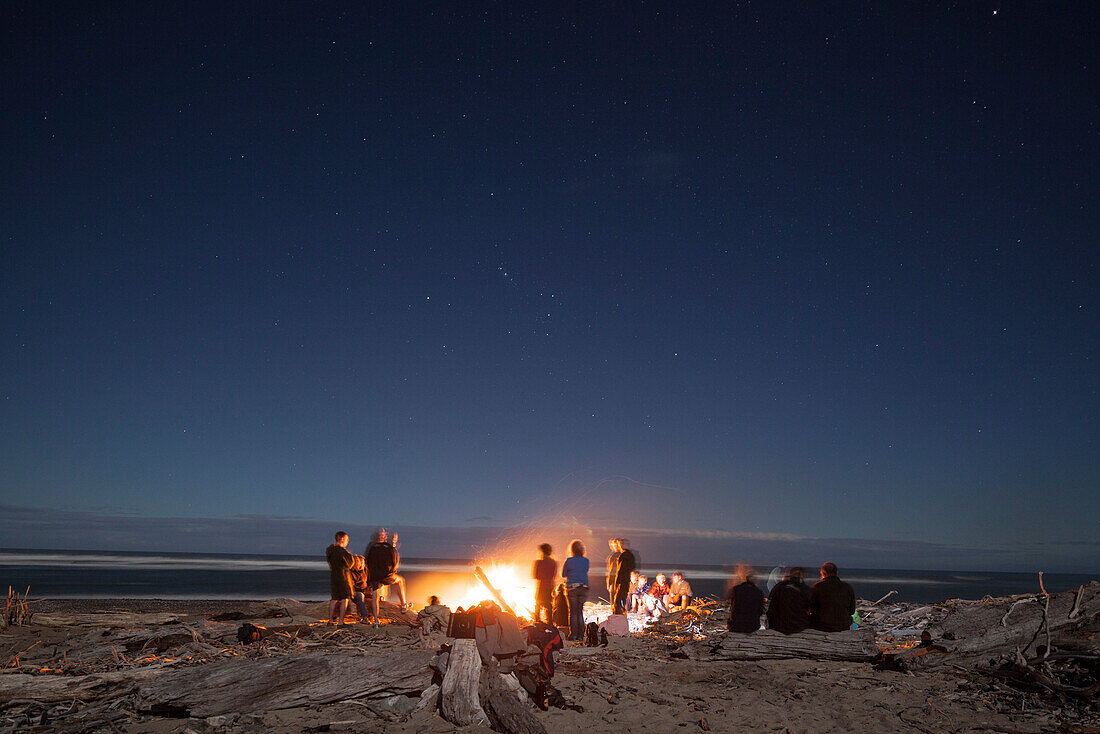 Lagerfeuer am Strand,Gruppe Menschen schart sich um offenes Feuer am Strand unter Sternhimmel,Westküste,Südinsel,Neuseeland